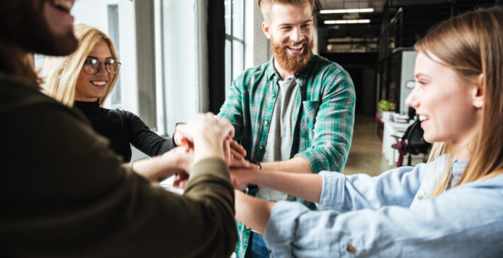 Image of young colleagues in office holding hands of each other. Looking aside.