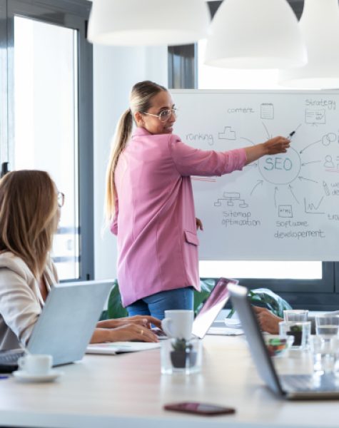 Shot of elegant young businesswoman pointing at white blackboard and explain a project to her colleagues on coworking place.