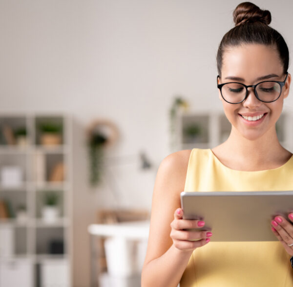 Smiling young project manager in eyeglasses using digital tablet while working with online platforms