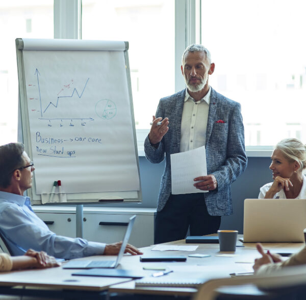 Confident mature businessman giving a presentation, explaining something to colleagues while having a meeting in the office. Business people working together